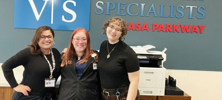 Three smiling employees pose together in front of a Veterinary Specialists sign in a hospital lobby