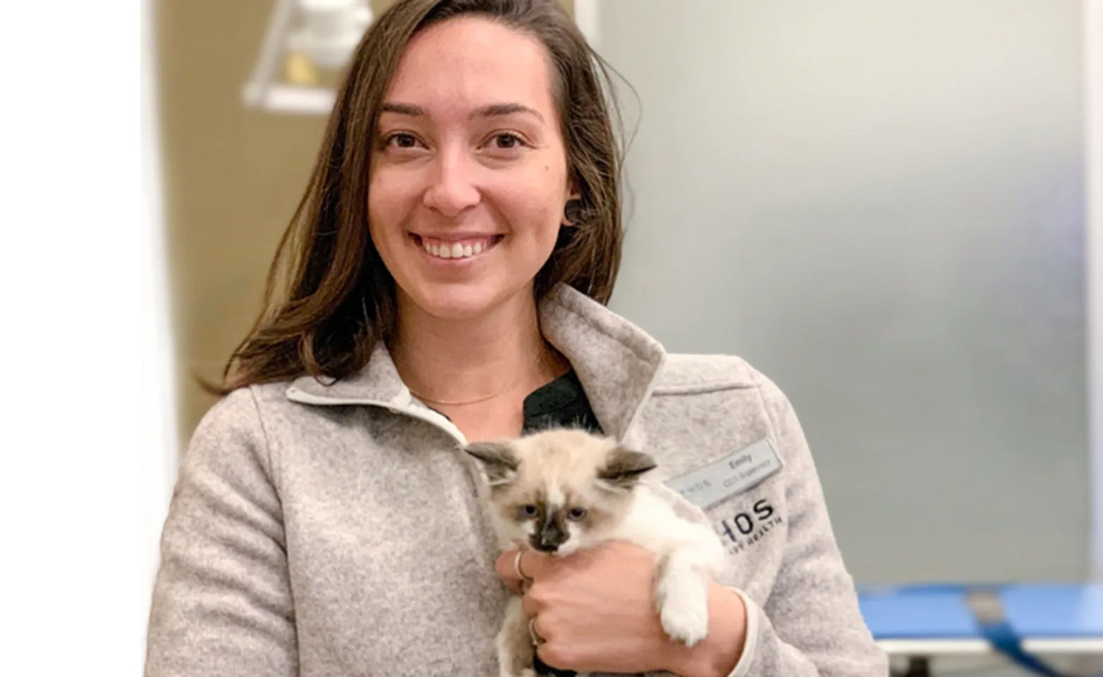 An Ethos veterinary professional smiling and holding a kitten An Ethos veterinary professional smiling and holding a kitten