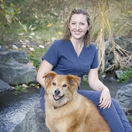 Dr. Cassie Henry sitting on a rock with an orange dog in front