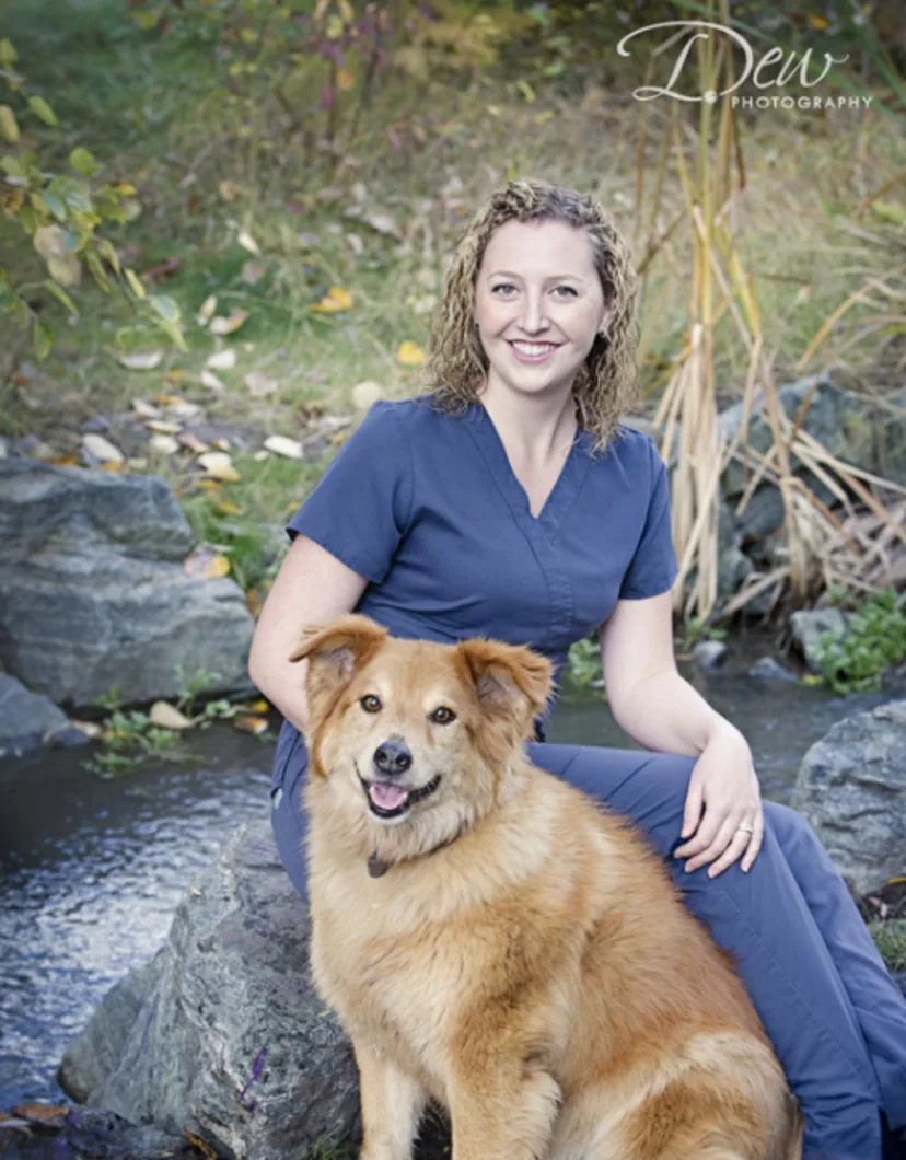 Dr. Cassie Henry sitting on a rock with an orange dog in front