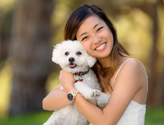 Woman posing for the camera with her little white poodle in a park.  They are both smiling. Woman posing for the camera with her little white poodle in a park.  They are both smiling.