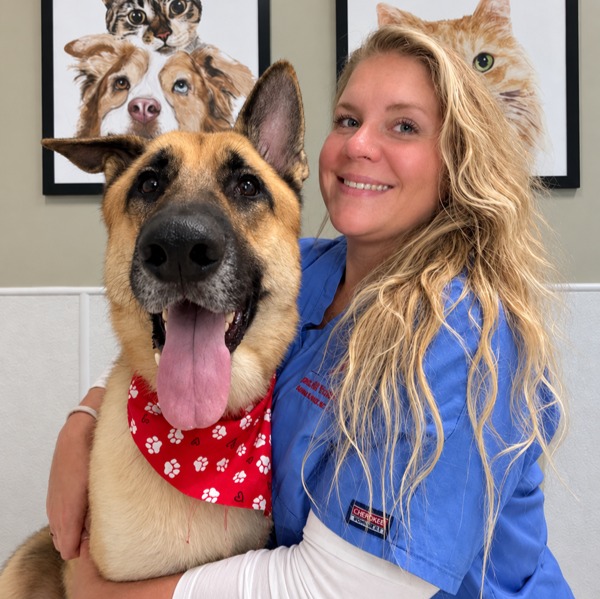 Jessica's staff photo from Spanish Trail Animal Hospital where she is outside on the lawn posing for a picture with a black dog next to her.