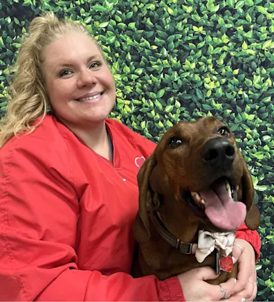 Jessica's staff photo from Spanish Trail Animal Hospital where she is outside on the lawn posing for a picture with a black dog next to her.