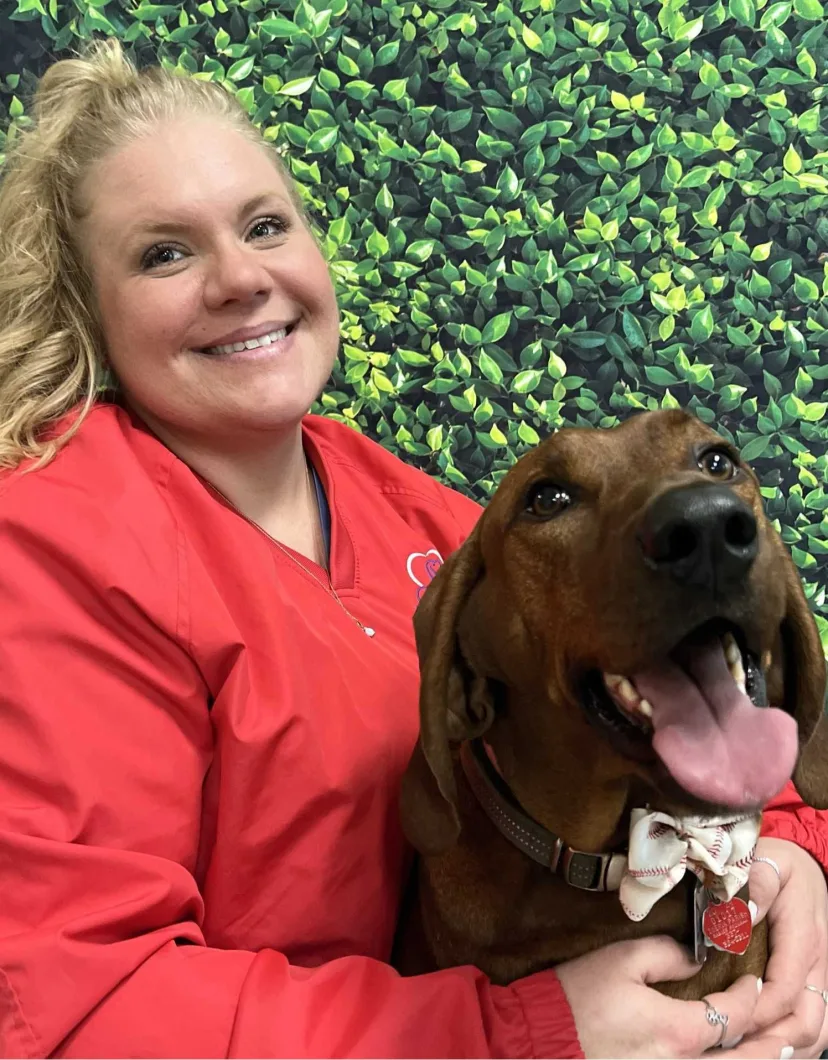 Jessica's staff photo from Spanish Trail Animal Hospital where she is outside on the lawn posing for a picture with a black dog next to her.