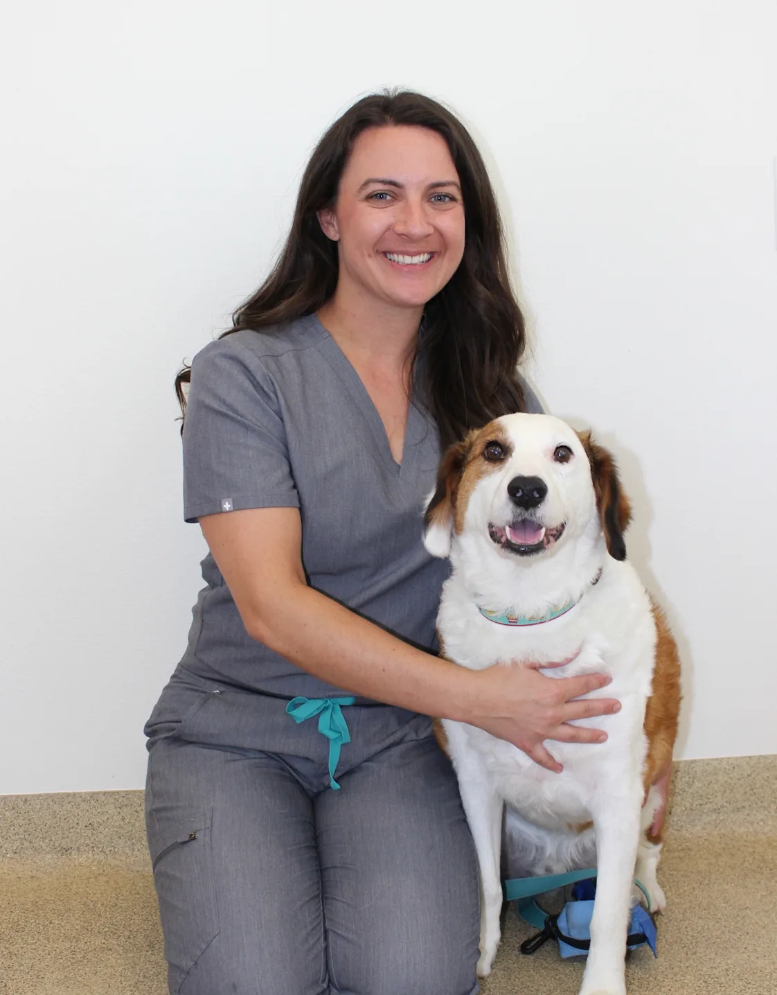 Dr. Kelly Schwaner smiling kneeling down next to a brown and white dog Dr. Kelly Schwaner smiling kneeling down next to a brown and white dog