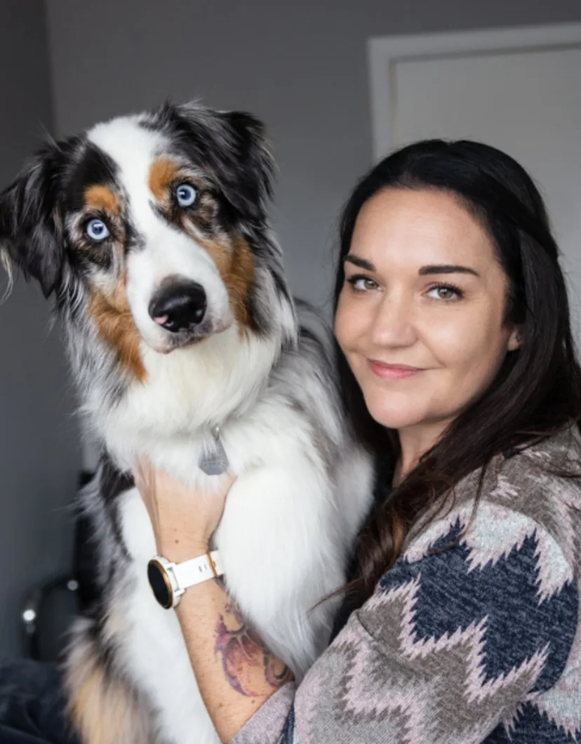 Lauren holding a black, white, and tan dog with blue eyes