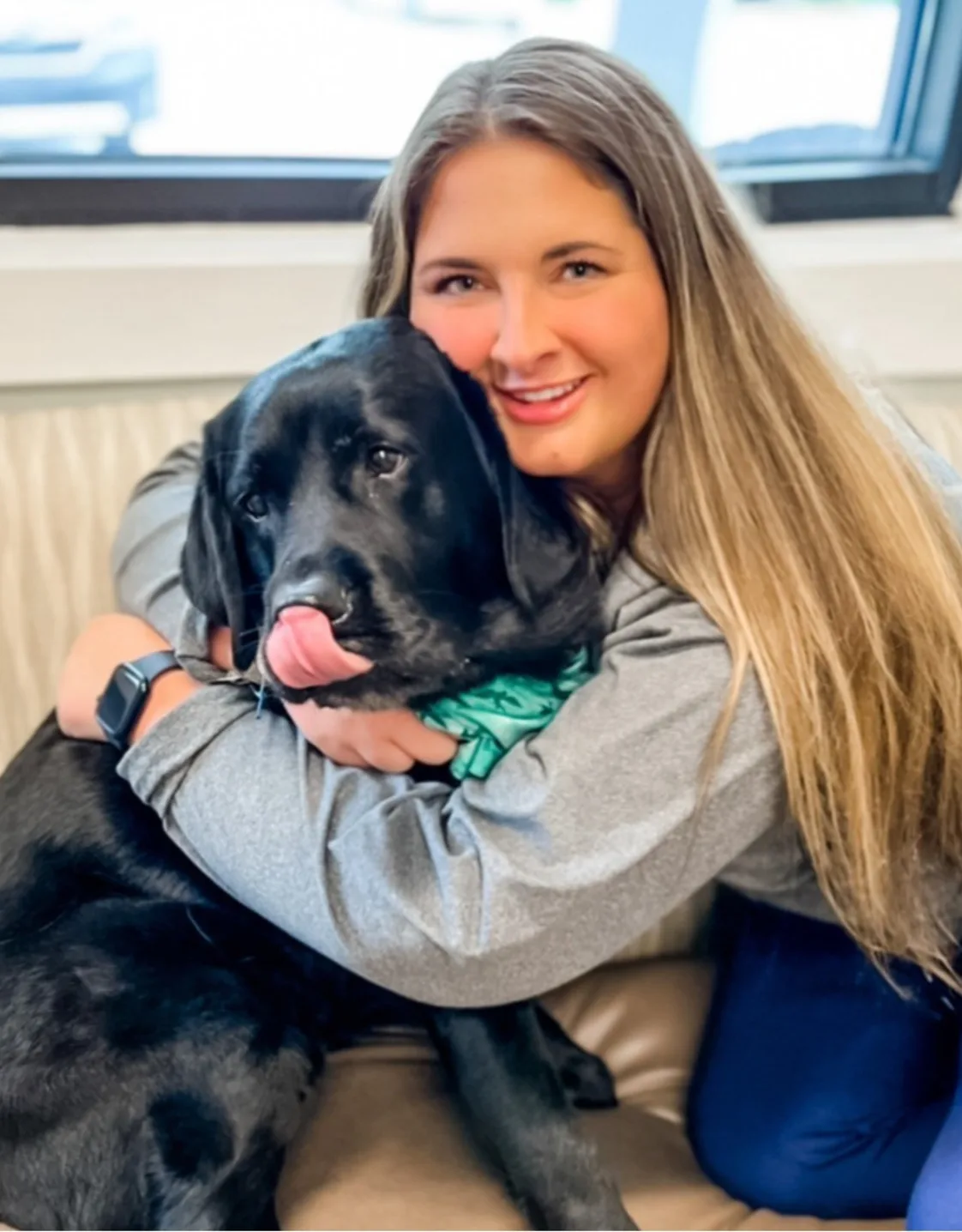 Rachel McIntyre smiling hugging a Black Lab sitting on waiting bench Rachel McIntyre smiling hugging a Black Lab sitting on waiting bench
