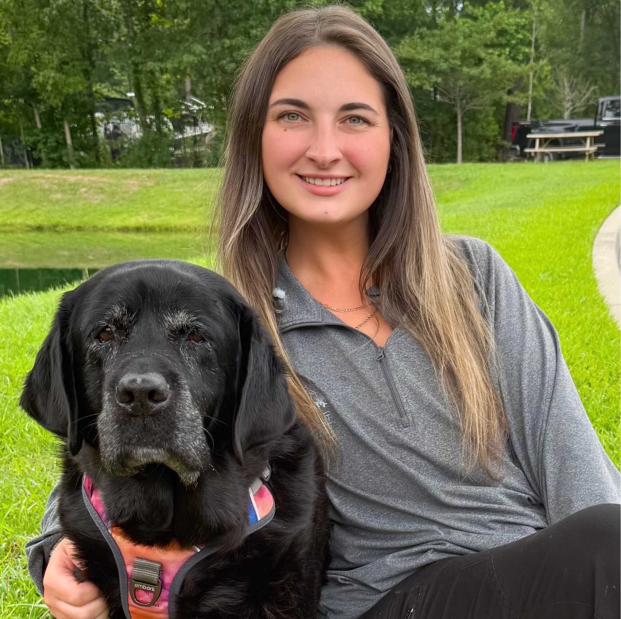 Rachel McIntyre smiling hugging a Black Lab sitting on waiting bench