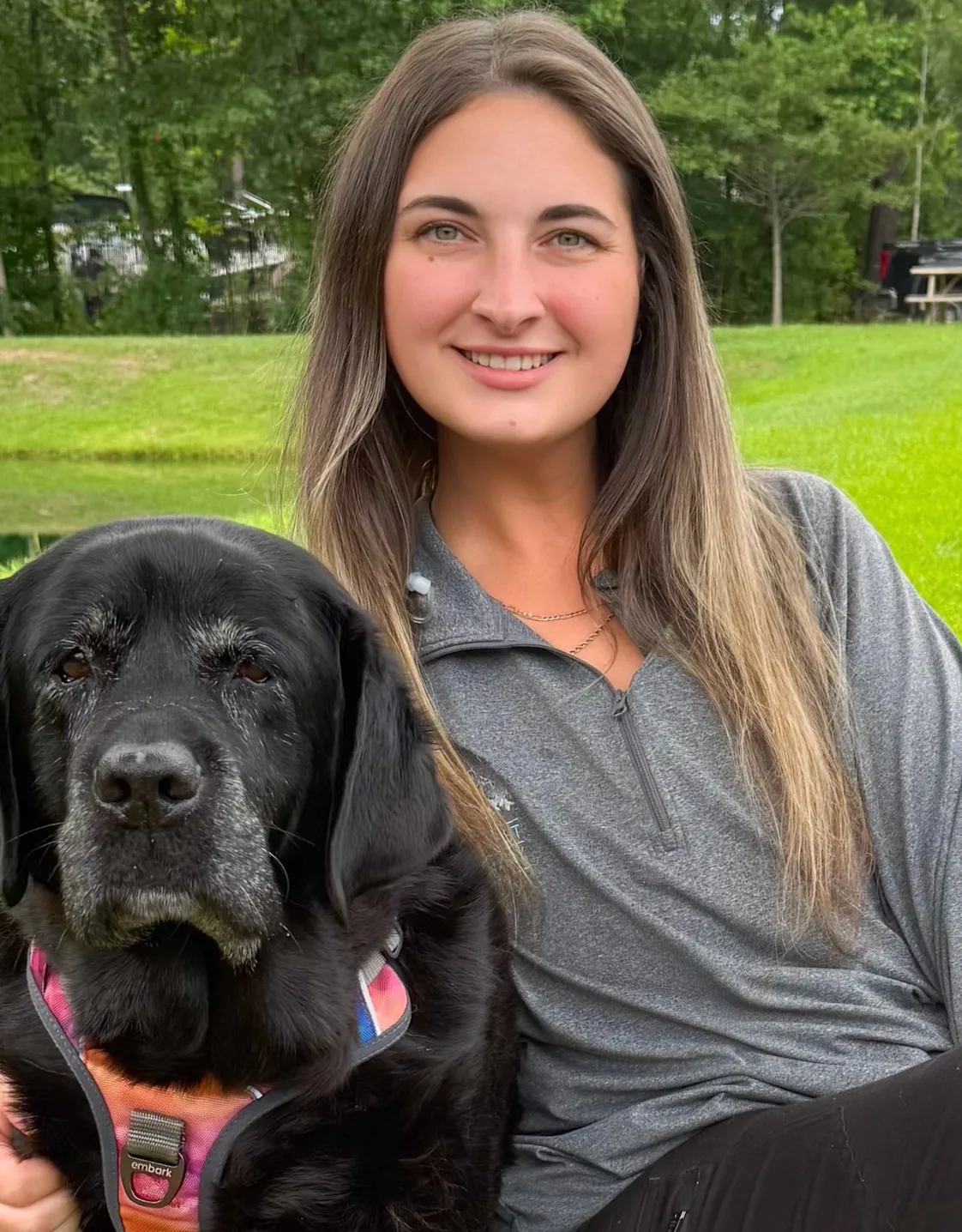 Rachel McIntyre smiling hugging a Black Lab sitting on waiting bench Rachel McIntyre smiling hugging a Black Lab sitting on waiting bench