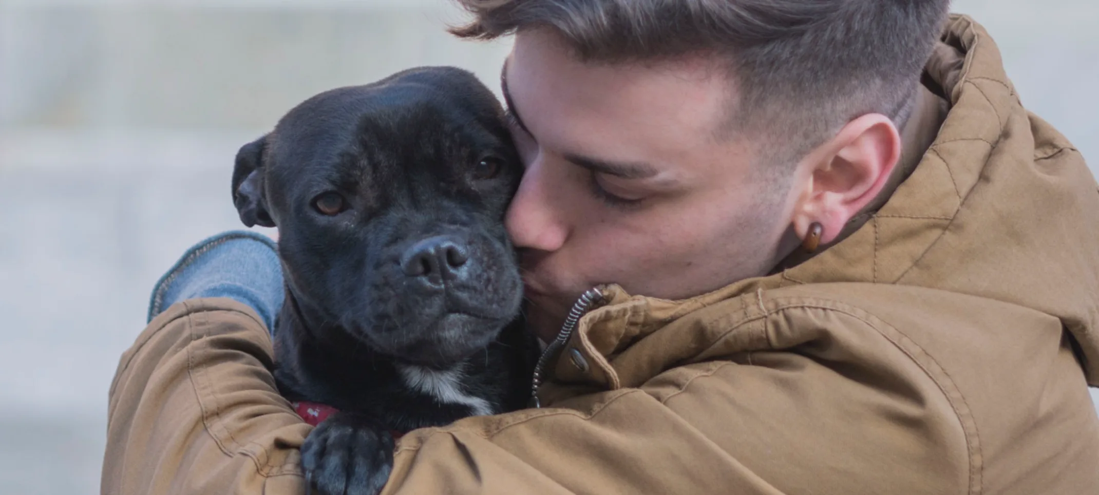 Gentleman is sitting on the ground hugging and kissing his black puppy lovingly.