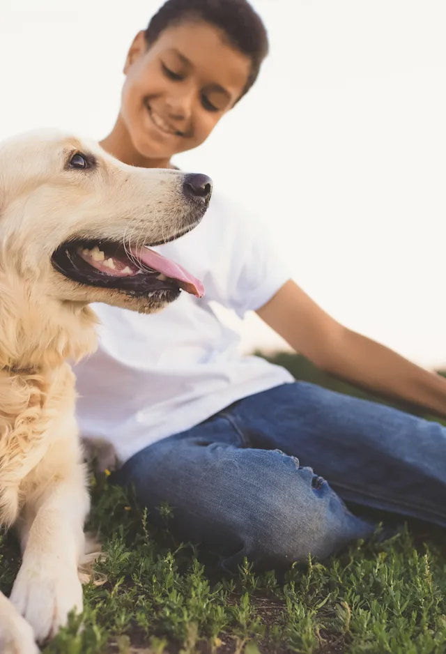 Little boy sitting on grass with his dog laying down next to him as he pets the top of his dogs head. Little boy sitting on grass with his dog laying down next to him as he pets the top of his dogs head.