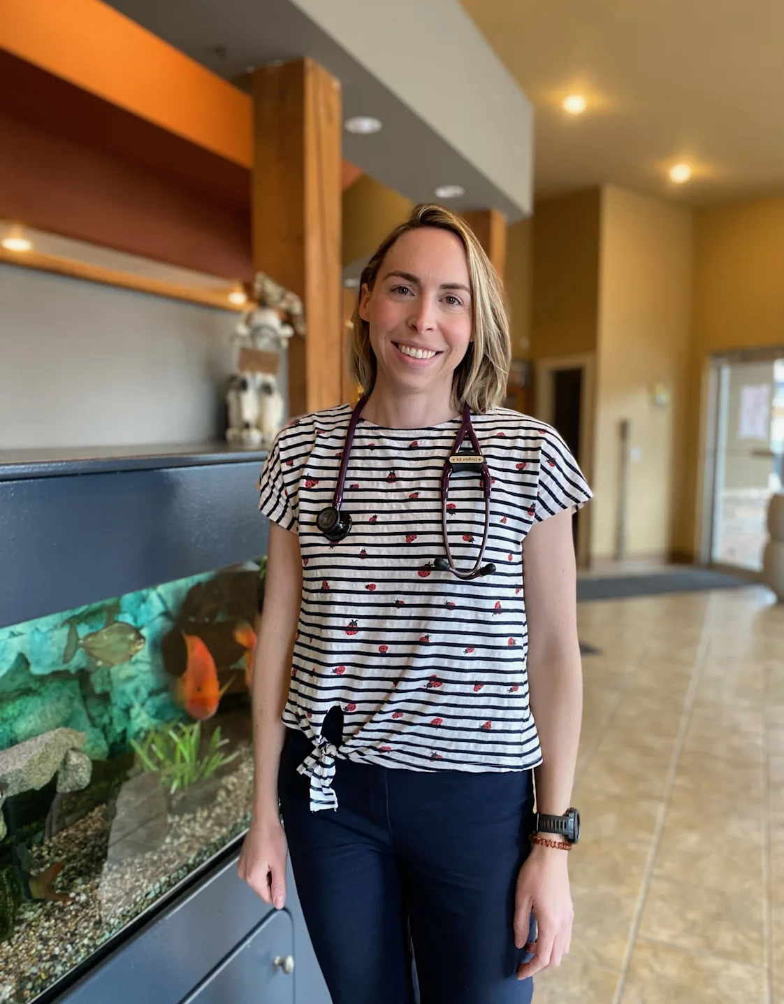 Dr. Courtney Ek smiling standing next to an aquarium Dr. Courtney Ek smiling standing next to an aquarium