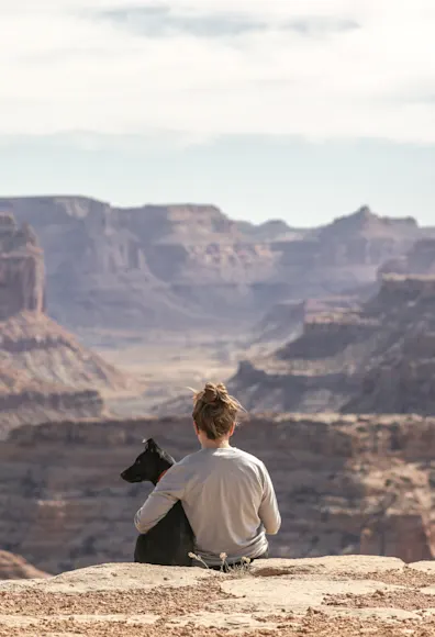 Dog and person sitting on the edge of a cliff starring at the canyon.