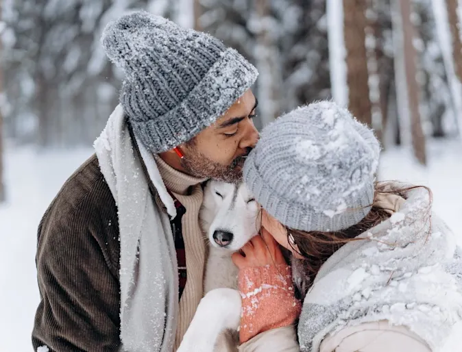 a man and woman embracing their dog outside in the snow a man and woman embracing their dog outside in the snow