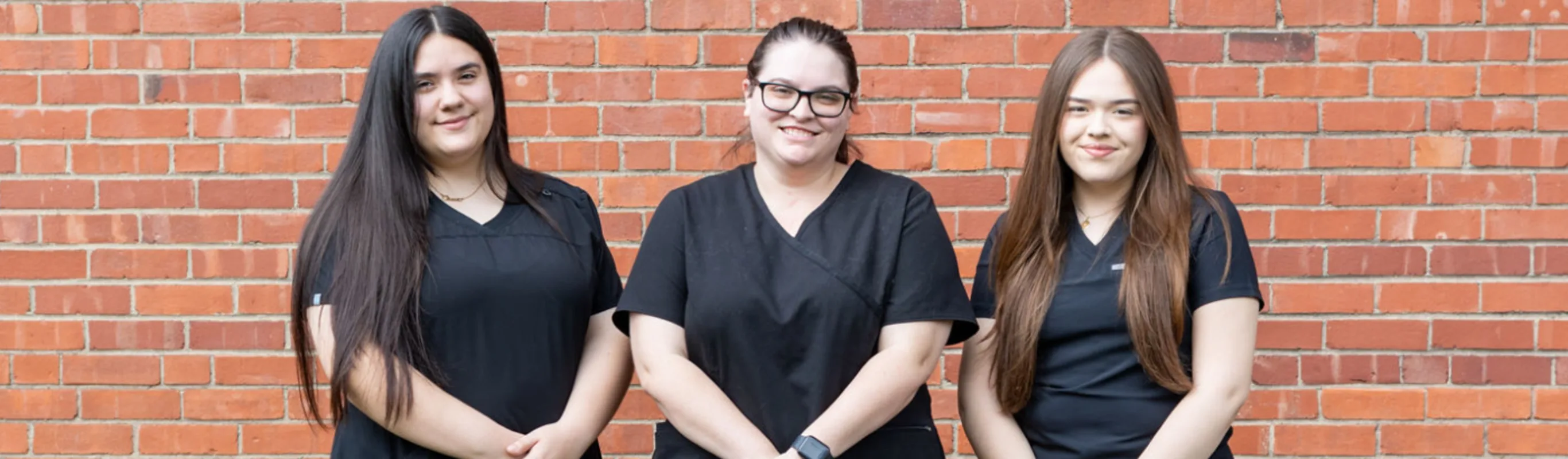 Three staff members in front of a brick wall Three staff members in front of a brick wall