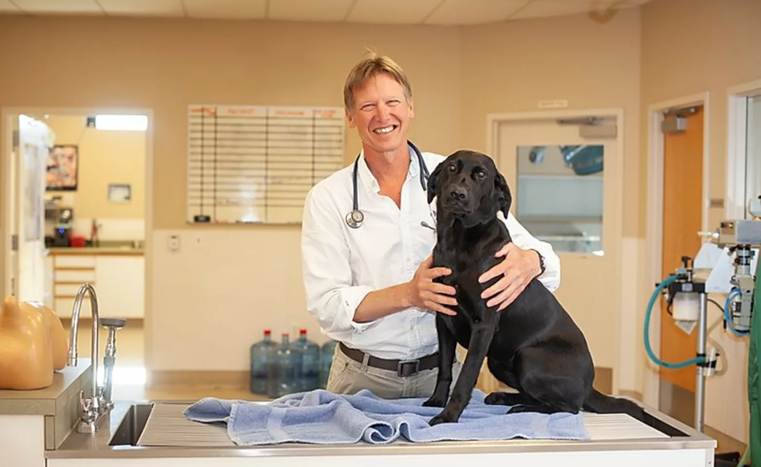 A doctor smiling and hugging a black dog