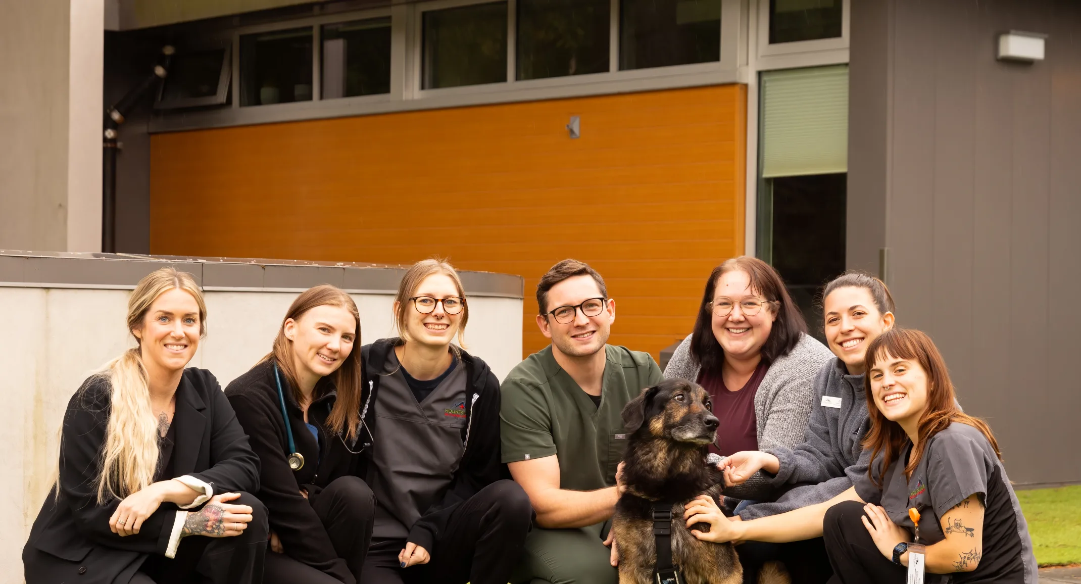 Staff kneeling down in a group around Charli outside in the grass Staff kneeling down in a group around Charli outside in the grass
