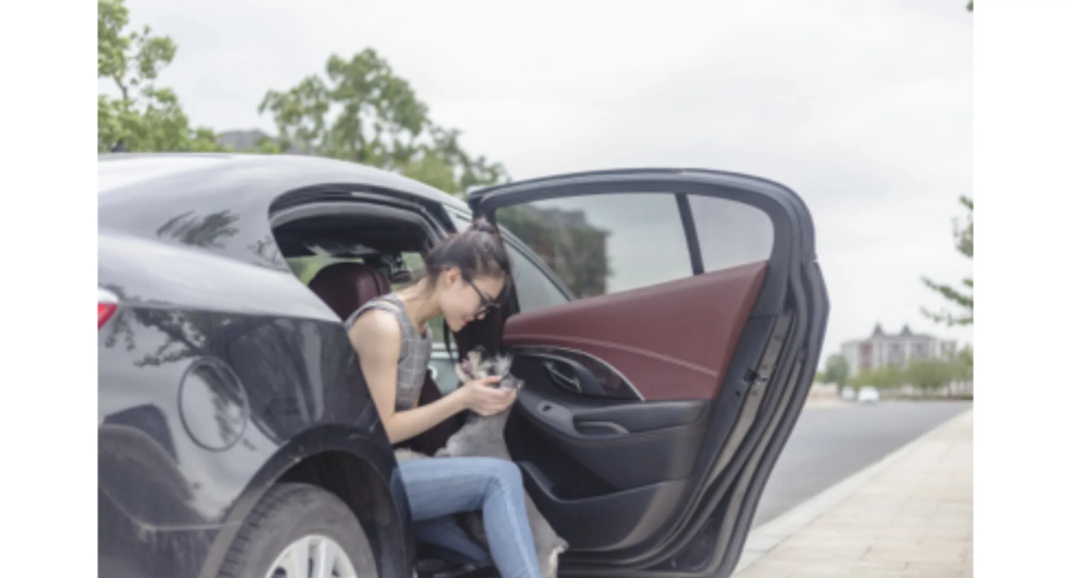 A girl with her dog, sitting in a parked car with the door open