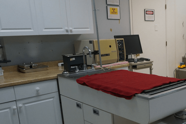 Strawbridge Animal Care's medical room 1 where there is table and a red towel on top of it.  There are medical equipment on a counter and computer in the room.