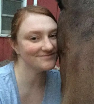 Kaycee leaned up against a brown horse's face