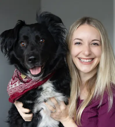 Hannah holding a black and white dog with a red bandana on