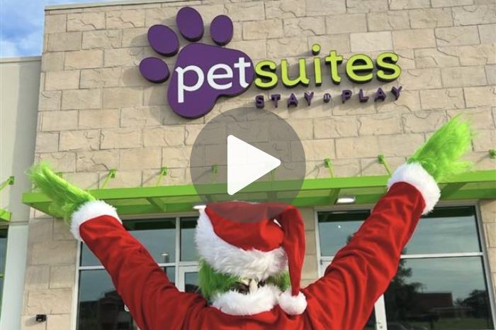 A person dressed as the grinch poses in front of a PetSuites location. 