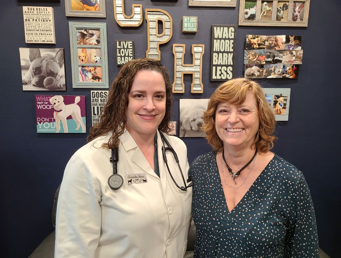 Dr. Amanda Maus and Hospital Manager Elise pose in front of a wall with various pet photos and decor
