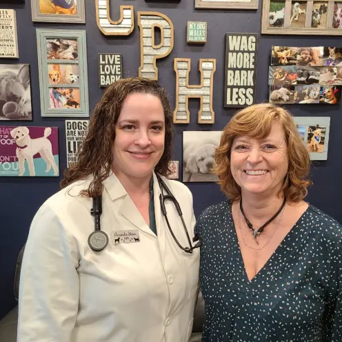 Dr. Amanda Maus and Hospital Manager Elise pose in front of a wall with various pet photos and decor