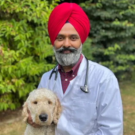 Dr. Mundi holding his small blond dog, Raavi, with trees in the background