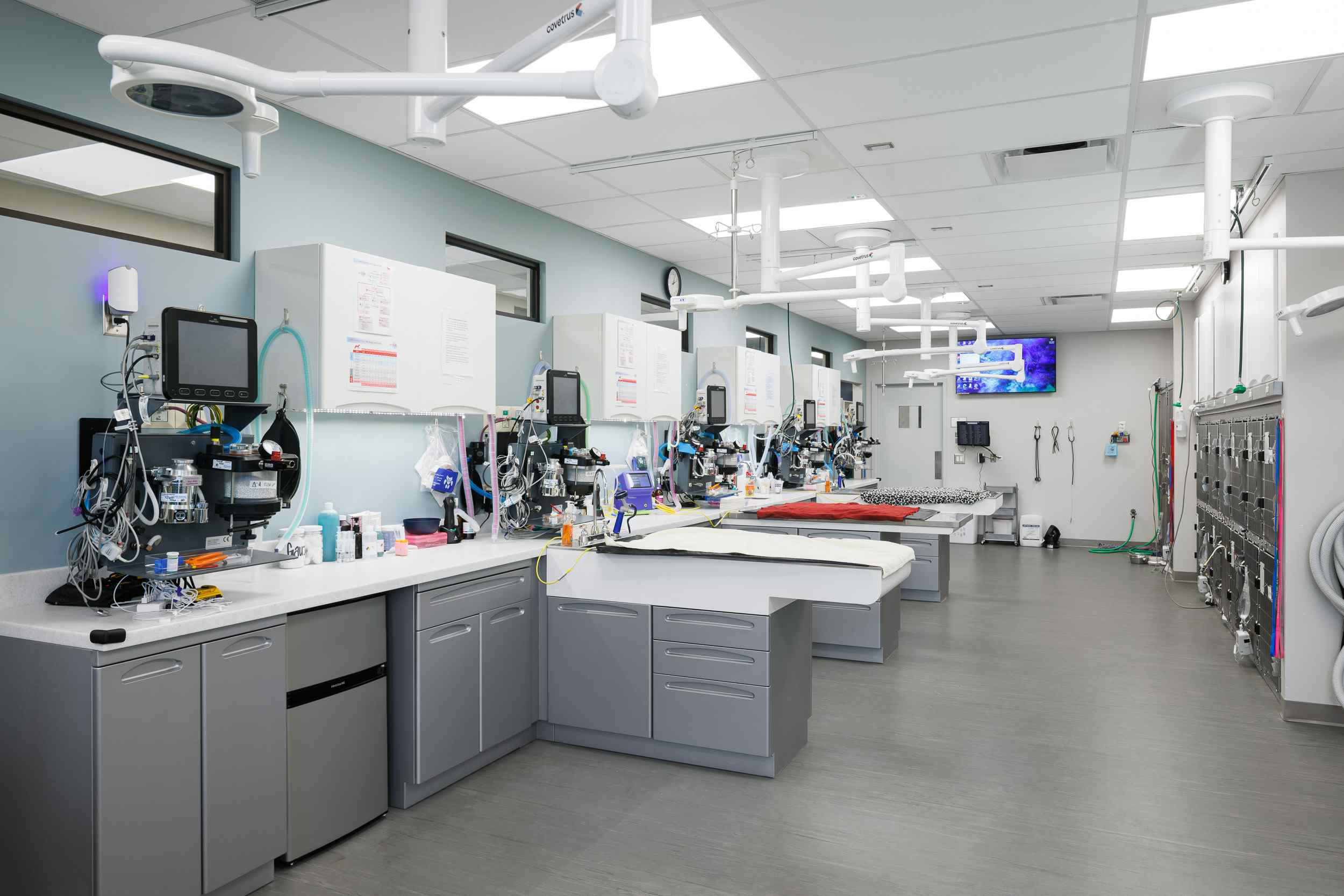 Operating tables in a backroom with medical equipment sitting on the counters.