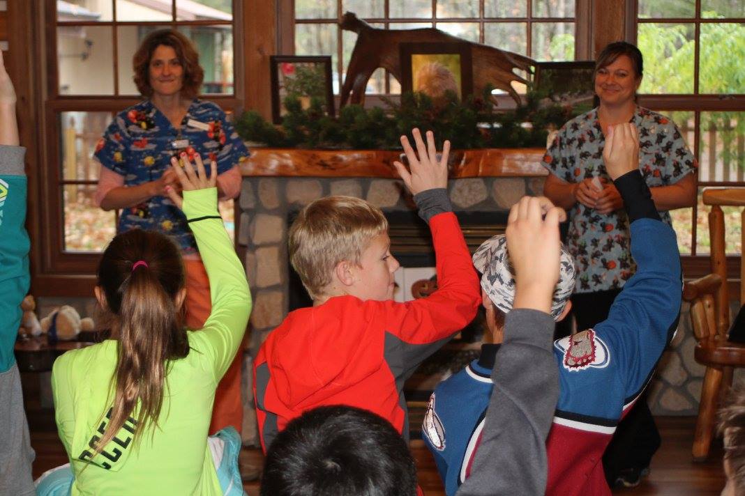 Two members of staff at All Creatures Veterinary Clinic giving a talk to some children with their hands raised