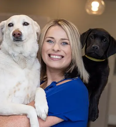 Katie smiling with a golden haired dog and a black dog behind her. Katie smiling with a golden haired dog and a black dog behind her.