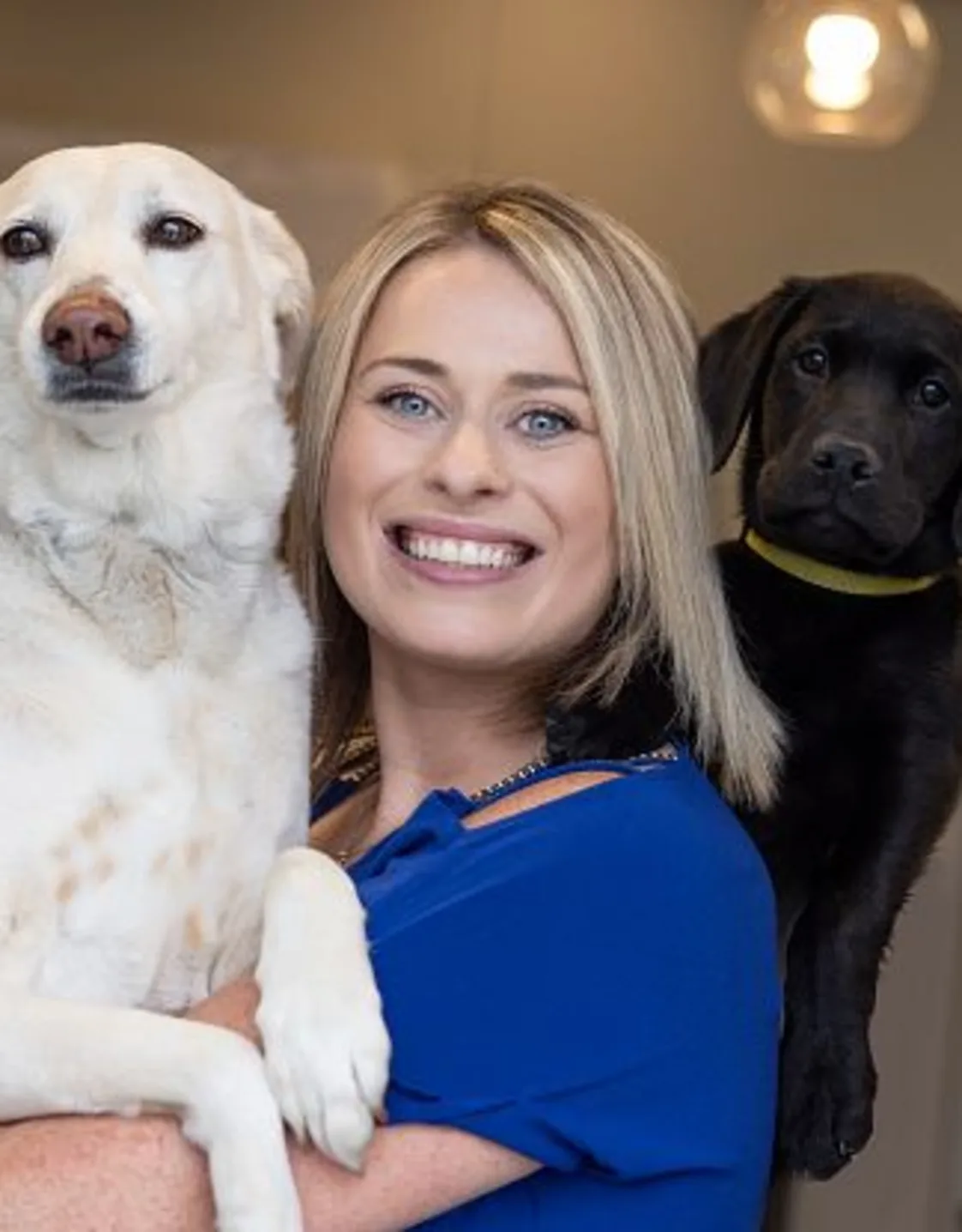Katie smiling with a golden haired dog and a black dog behind her. Katie smiling with a golden haired dog and a black dog behind her.