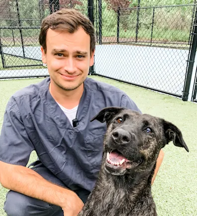 Nick Hepburn smiling kneeling down next to a large black and brown dog outside Nick Hepburn smiling kneeling down next to a large black and brown dog outside