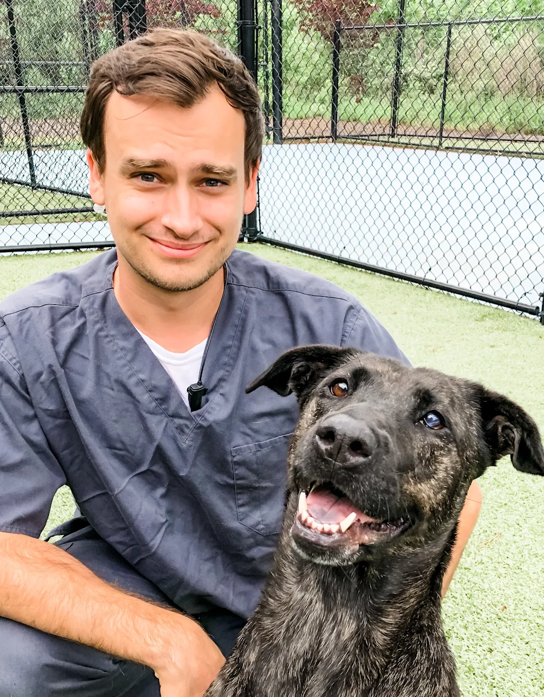 Nick Hepburn smiling kneeling down next to a large black and brown dog outside Nick Hepburn smiling kneeling down next to a large black and brown dog outside