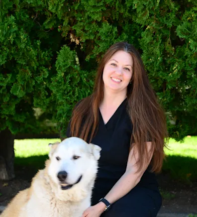 Becky holding a dog and sitting in front of the Eastside sign