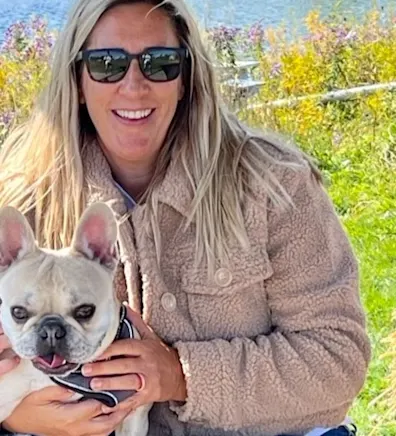 Eve smiling in front of a lake holding a small white dog Eve smiling in front of a lake holding a small white dog
