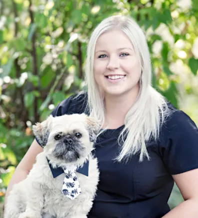 Nicole holding a little white dog with a tie on