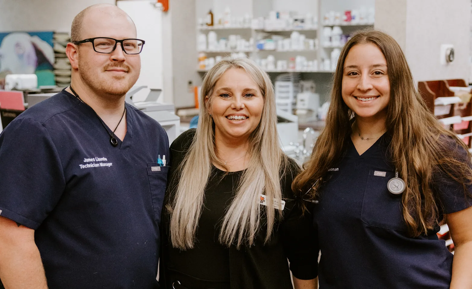 Three people in medical scrubs and casual attire stand together smiling in a clinic Three people in medical scrubs and casual attire stand together smiling in a clinic