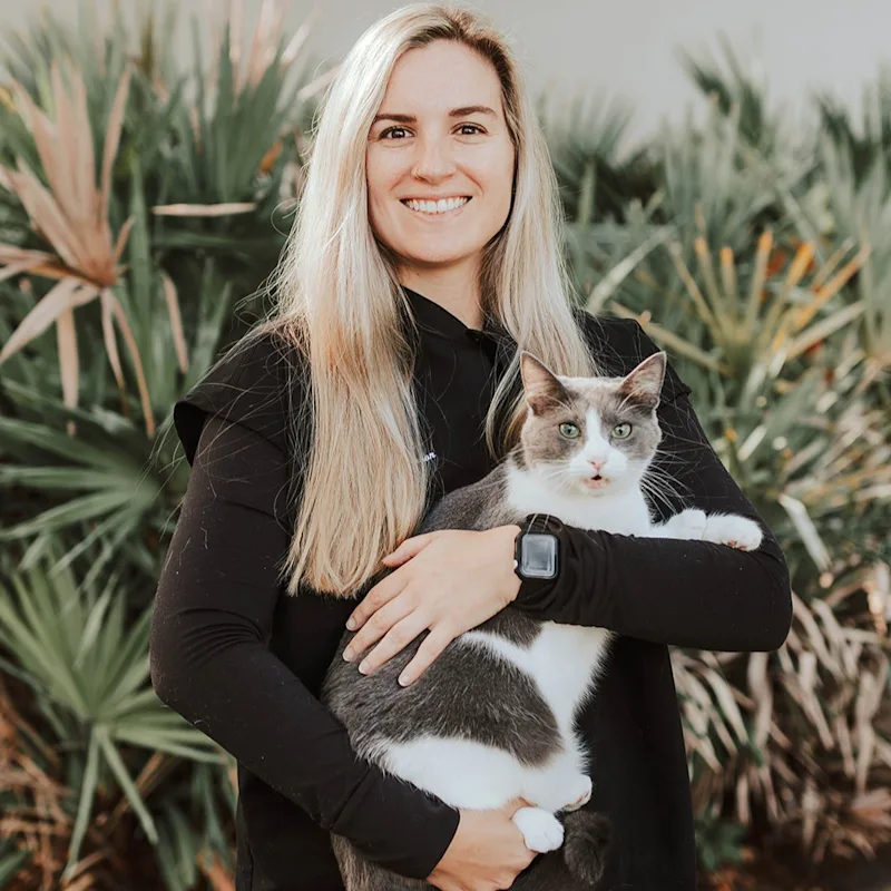 A photo of Dr. Tess Lawhon holding a calico cat named Cersei against a background of palm trees A photo of Dr. Tess Lawhon holding a calico cat named Cersei against a background of palm trees