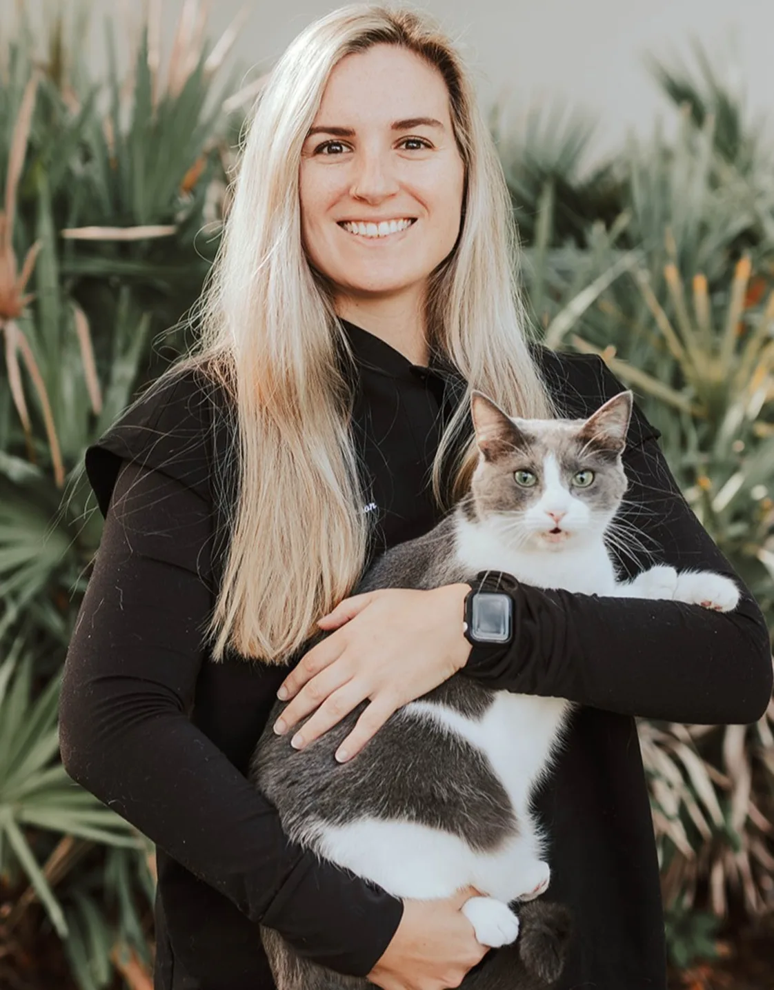 A photo of Dr. Tess Lawhon holding a calico cat named Cersei against a background of palm trees A photo of Dr. Tess Lawhon holding a calico cat named Cersei against a background of palm trees