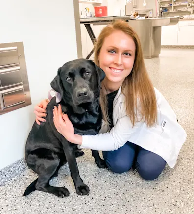 Dr. Tara Harasim smiling kneeling down next to a Black Lab Dr. Tara Harasim smiling kneeling down next to a Black Lab