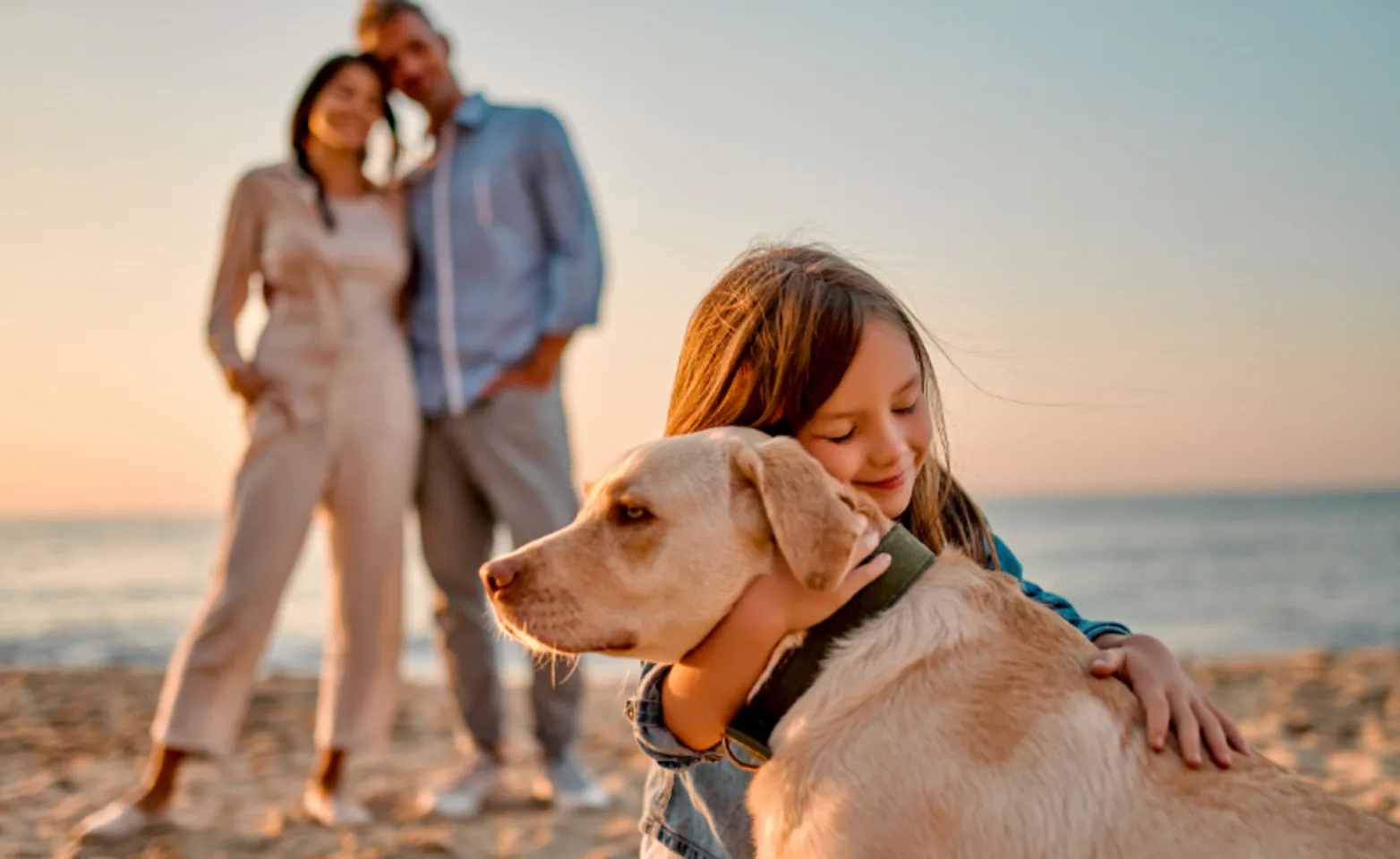 Girl Hugging Dog in Front of Her Parents at the Beach Girl Hugging Dog in Front of Her Parents at the Beach
