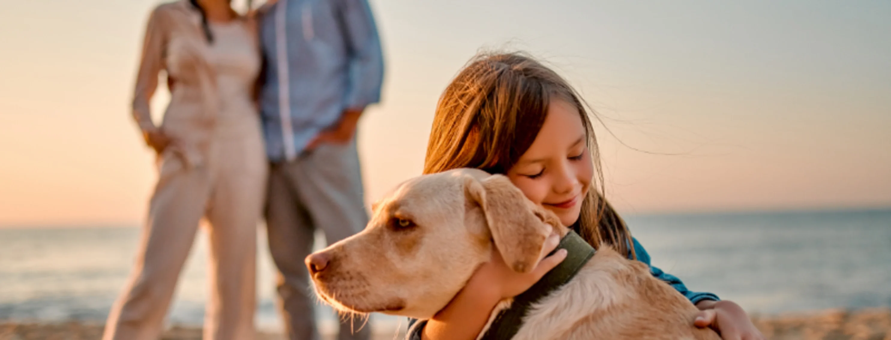 Girl Hugging Dog in Front of Her Parents at the Beach Girl Hugging Dog in Front of Her Parents at the Beach