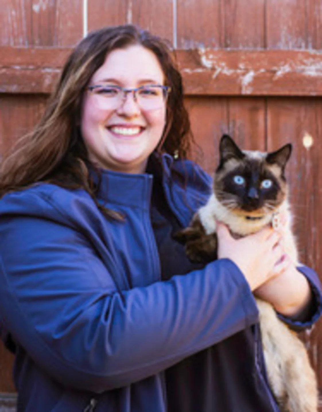 Laurynn standing in front of a wood fence holding a siamese cat Laurynn standing in front of a wood fence holding a siamese cat