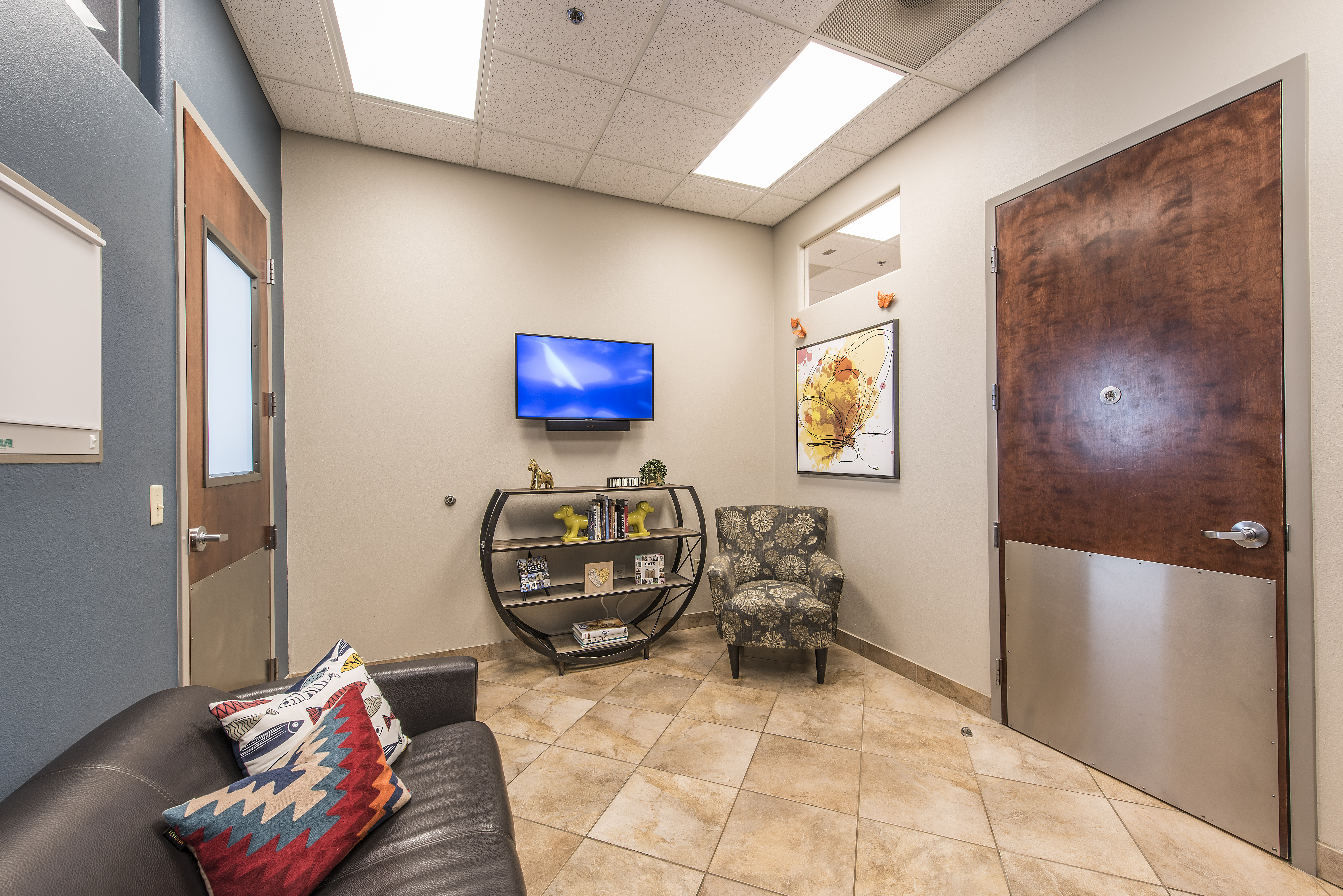 Hillside Animal Hospital Sitting Room that has TV mounted on the wall, chair and leather love seat to sit in. 
