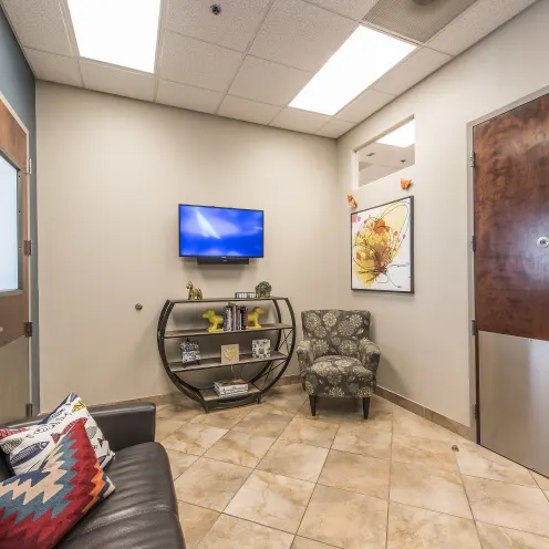 Hillside Animal Hospital Sitting Room that has TV mounted on the wall, chair and leather love seat to sit in. 