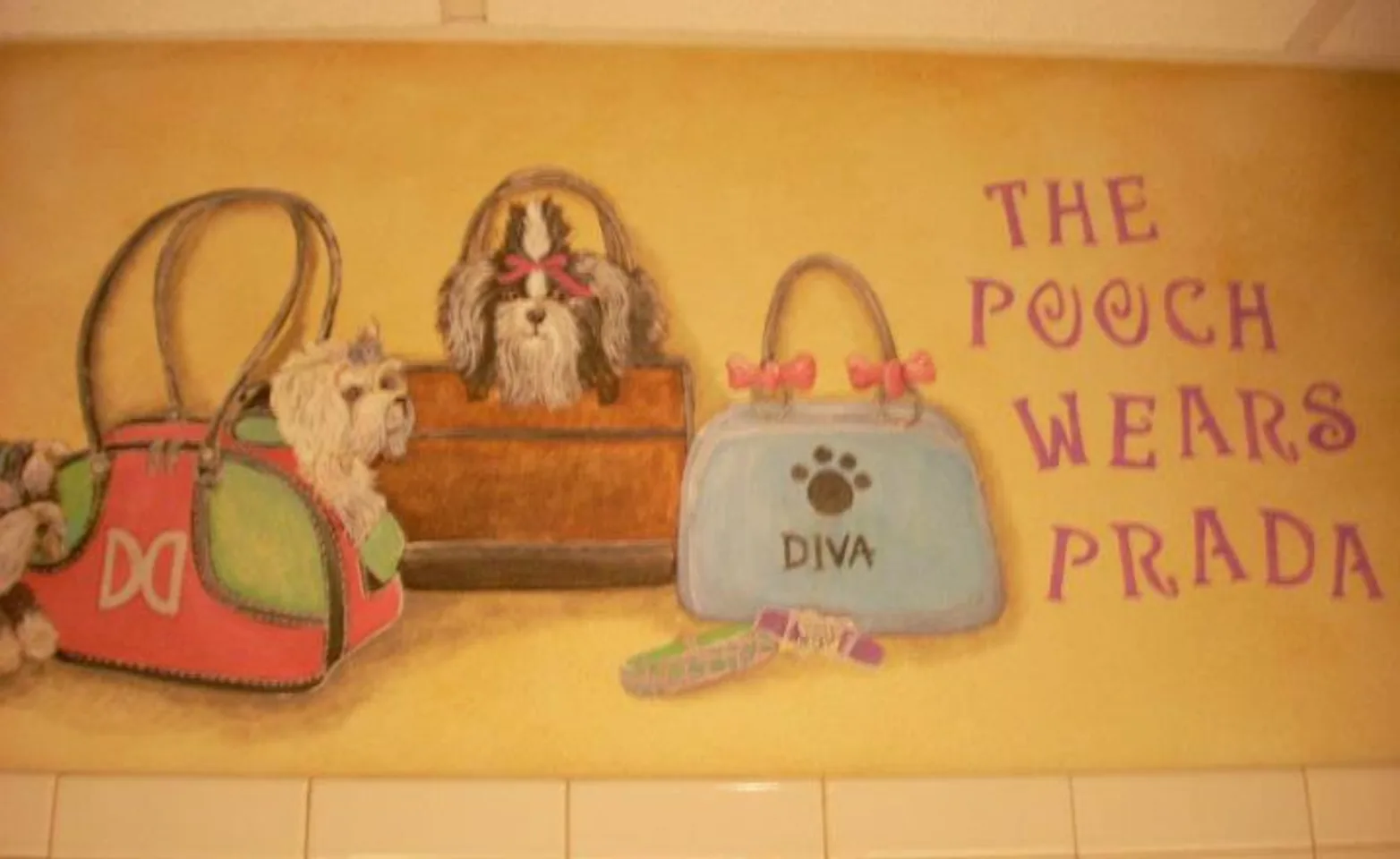 A painted mural of three small dogs sitting inside of three purses with the writing "THE POOCH WEARS PRADA" next to it