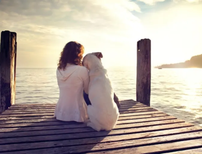 A woman and dog sit on a dock