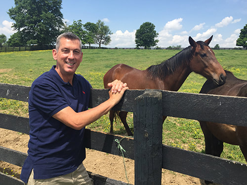 Dr. Browning, equine veterinarian, leaning on fence next to two brown horses